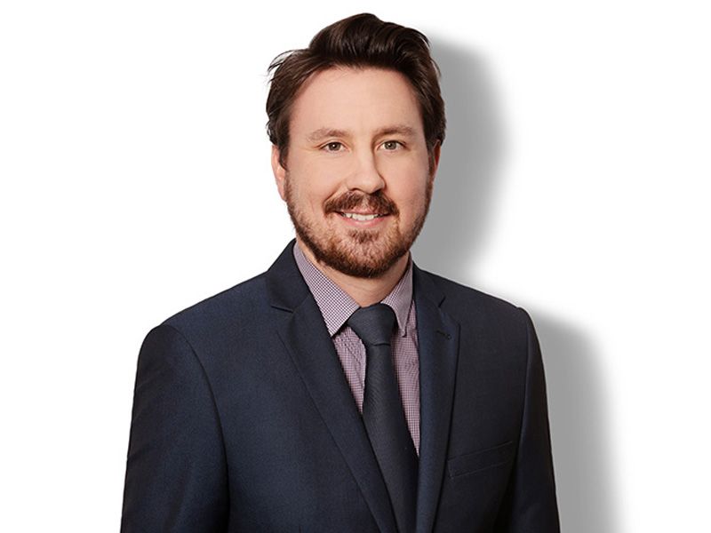 A man with a beard is wearing a suit and tie and smiling.