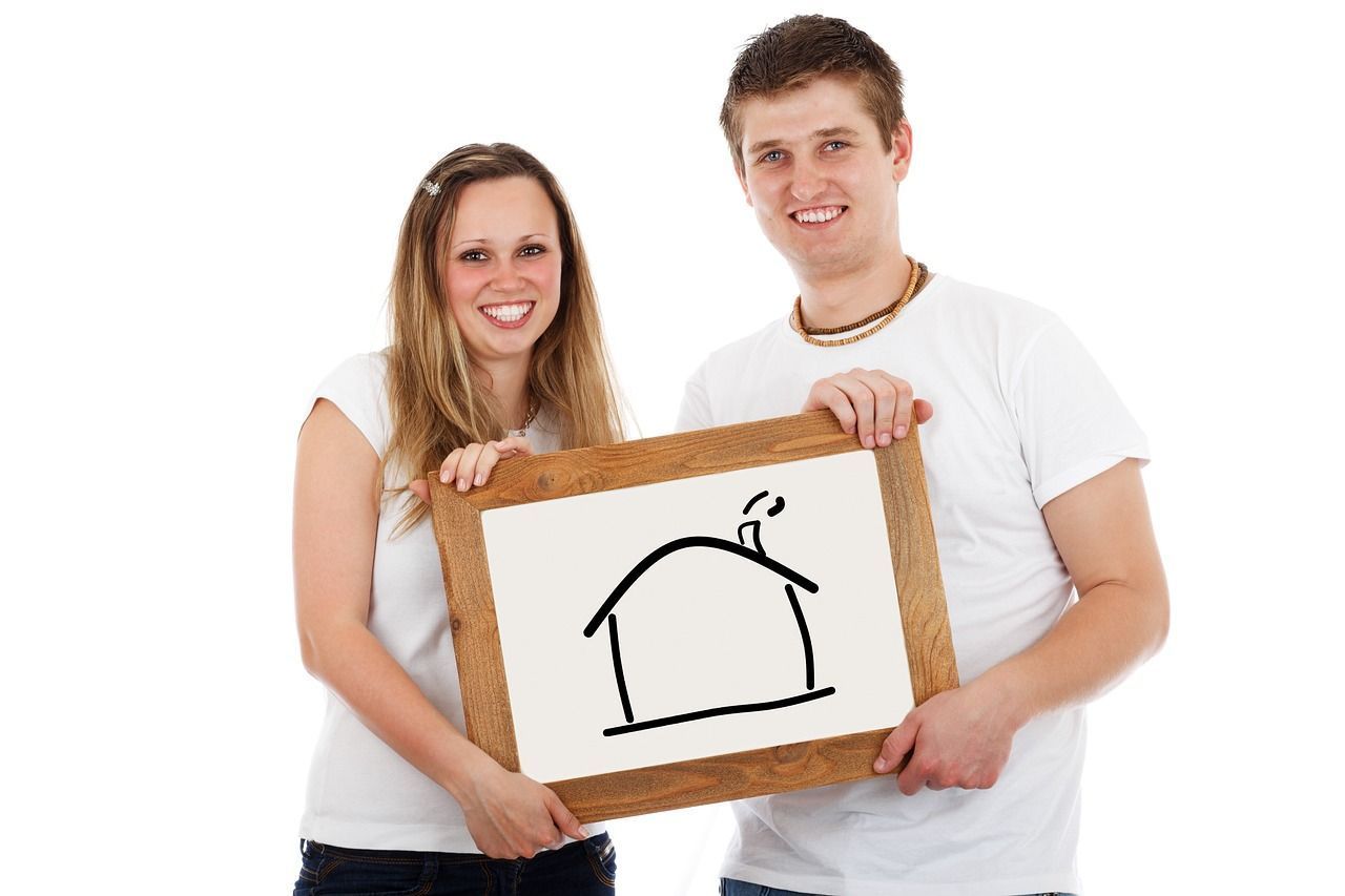 A couple holding up a drawing of a house in a whiteboard.