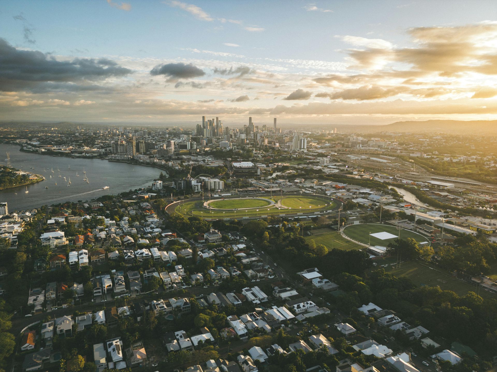 Aerial view of a city skyline, river, and oval sports field at sunset