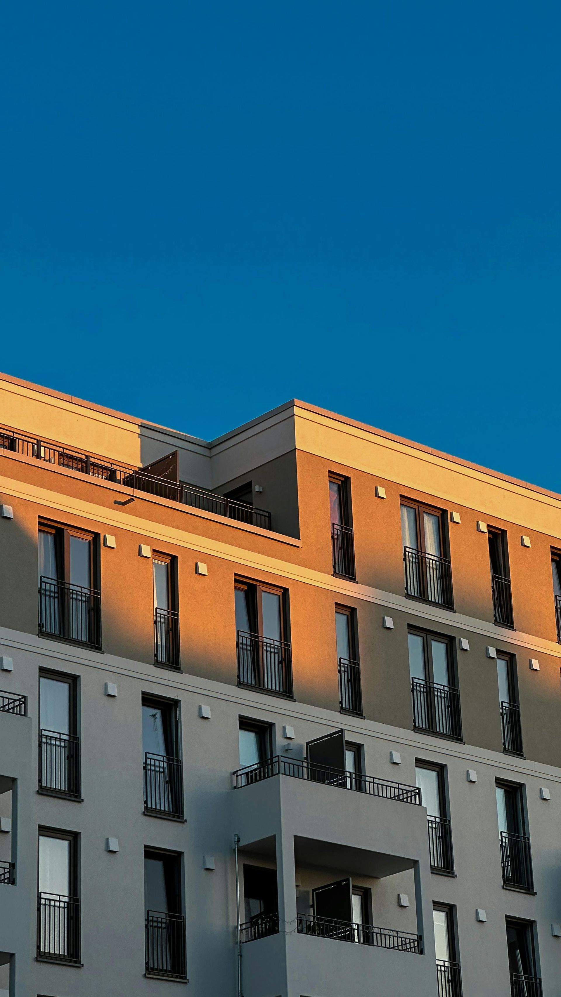 Modern apartment building with orange and gray facade against a clear blue sky