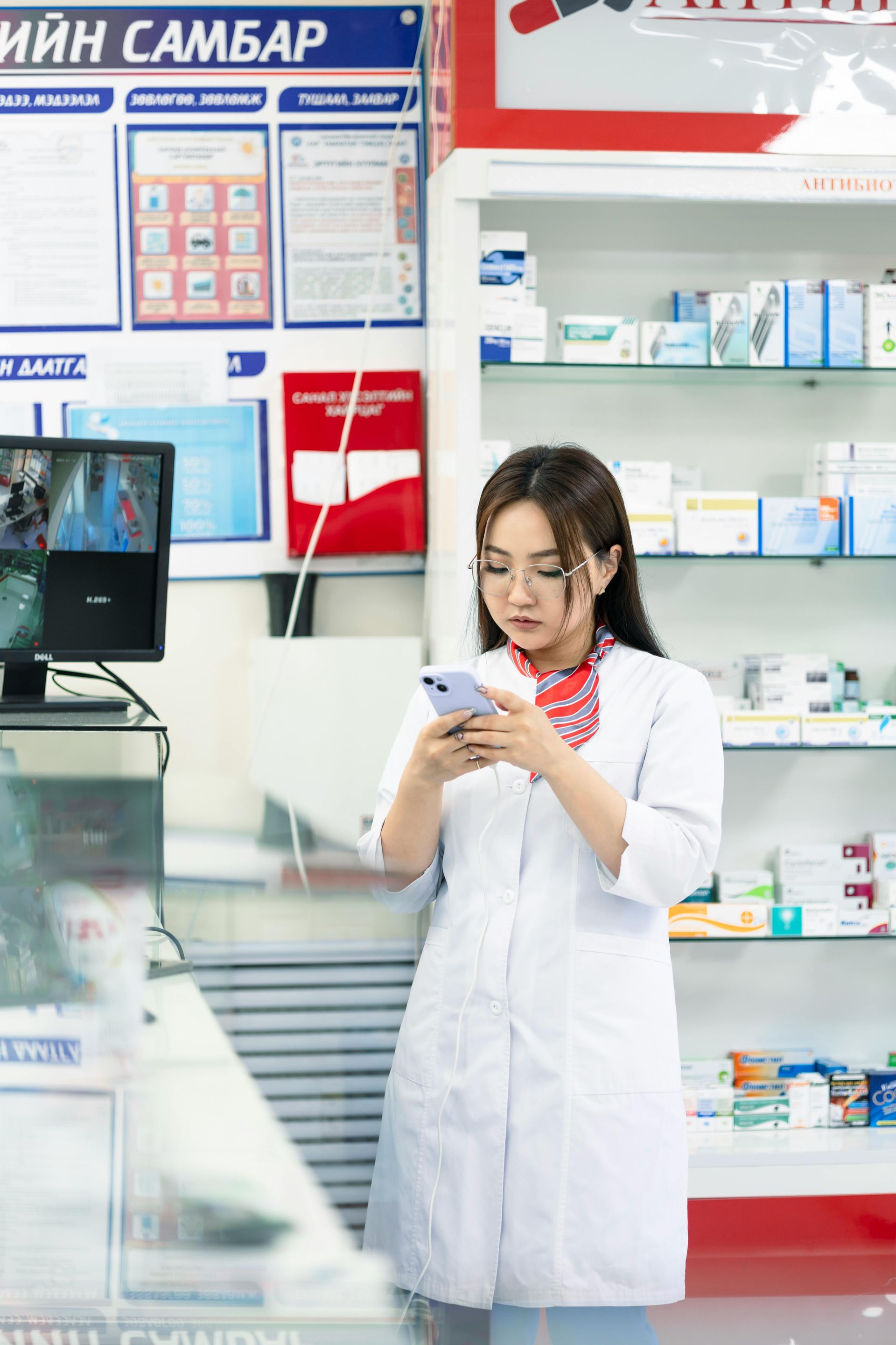 A female pharmacist standing behind counter and infront of medicine shelf.