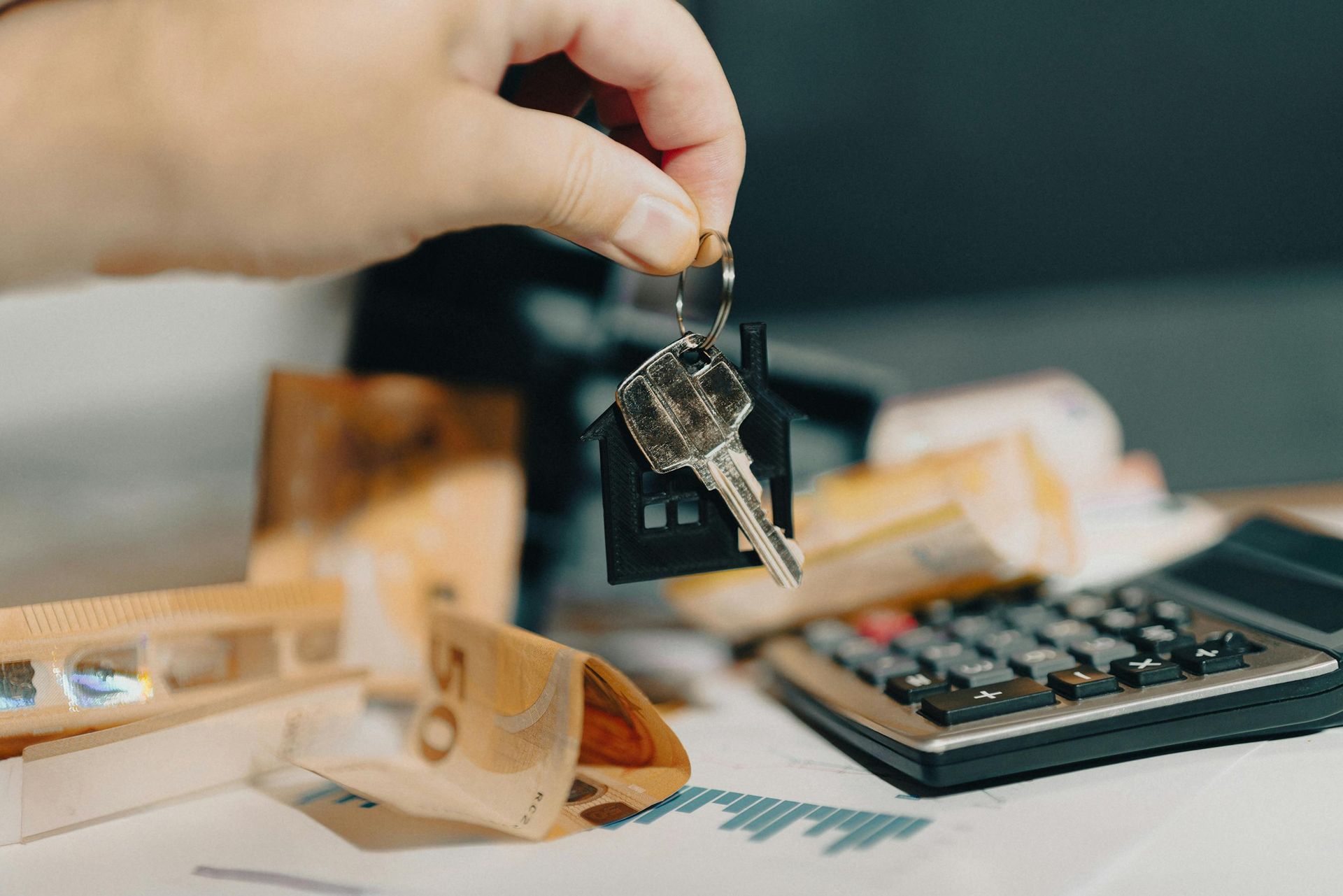 Hand holding car keys above scattered cash and a calculator on a desk