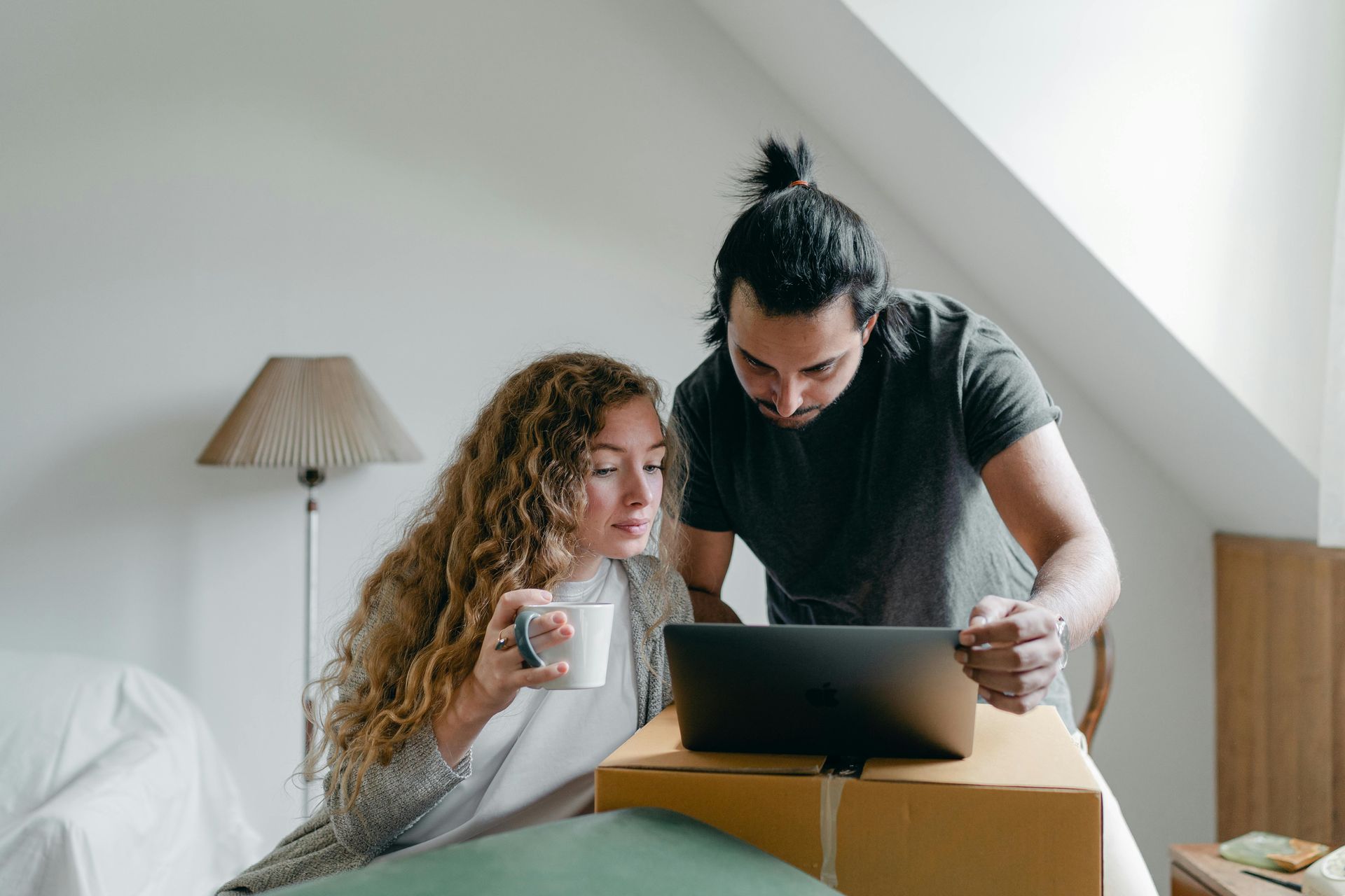 A couple looking a laptop, surrounded by house moving boxes.