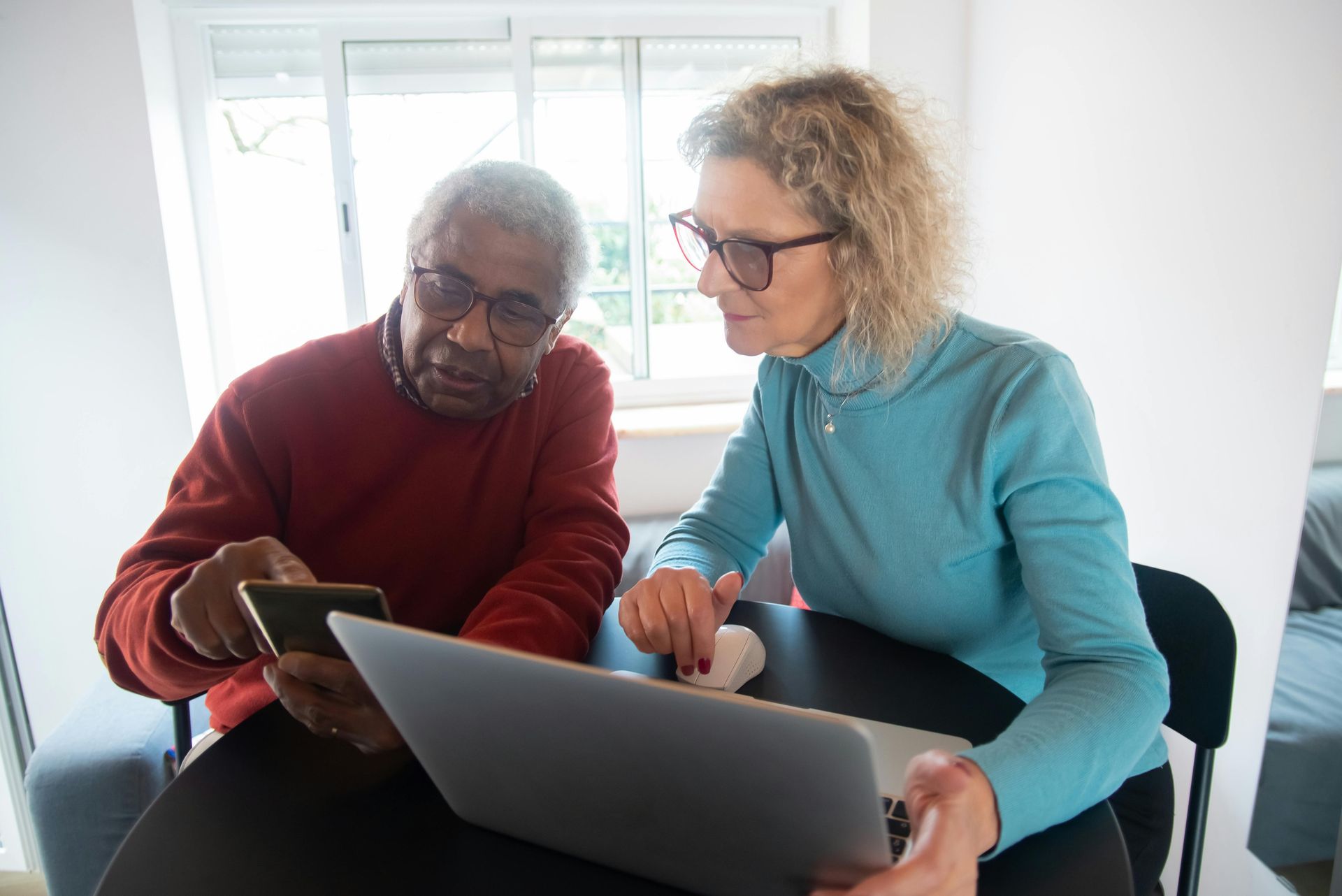 A female assisting a male retiree on a laptop.
