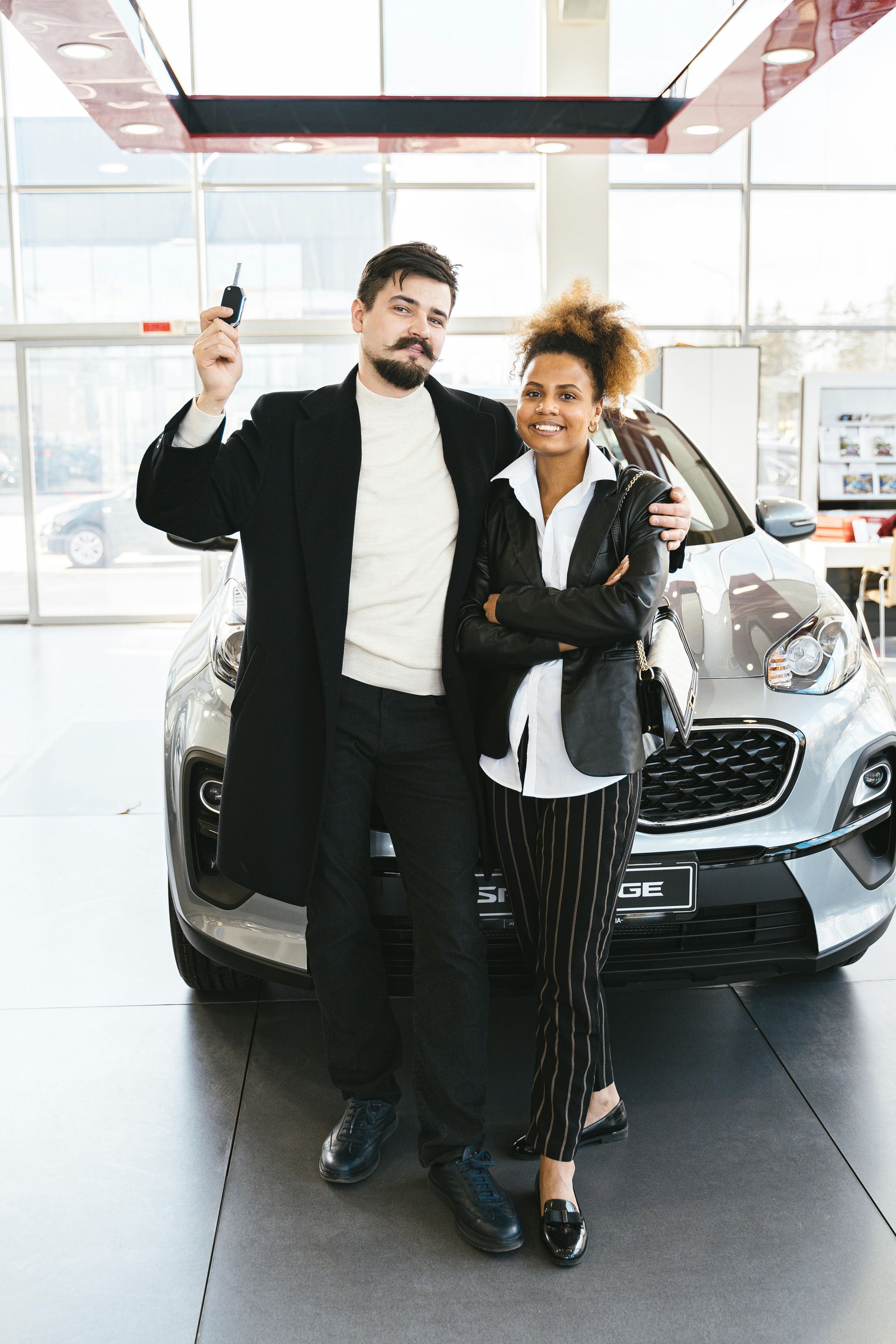 A couple standing and smiling in front of a car, with the man holding up car keys.