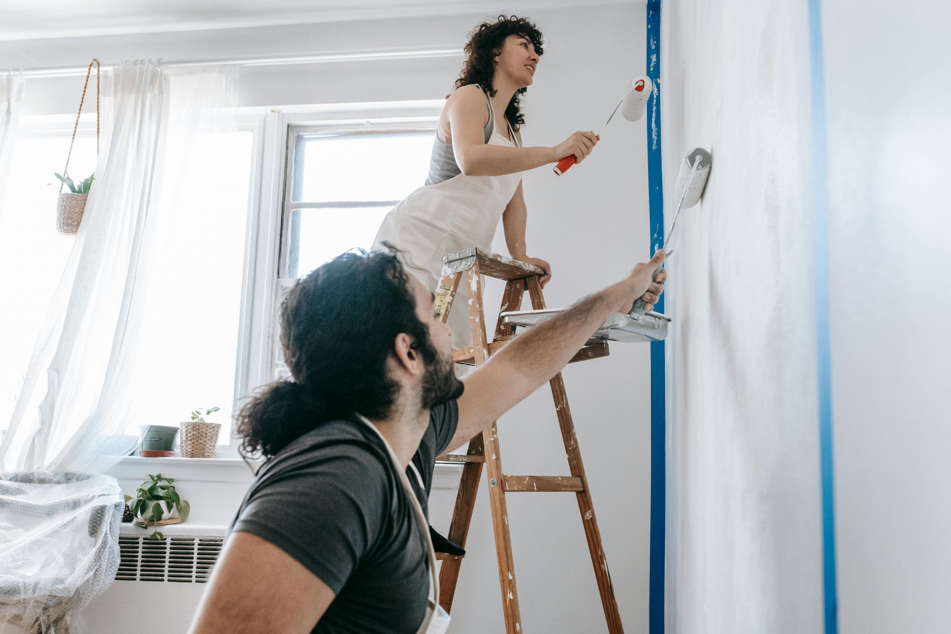 A couple painting a house wall with white paint.