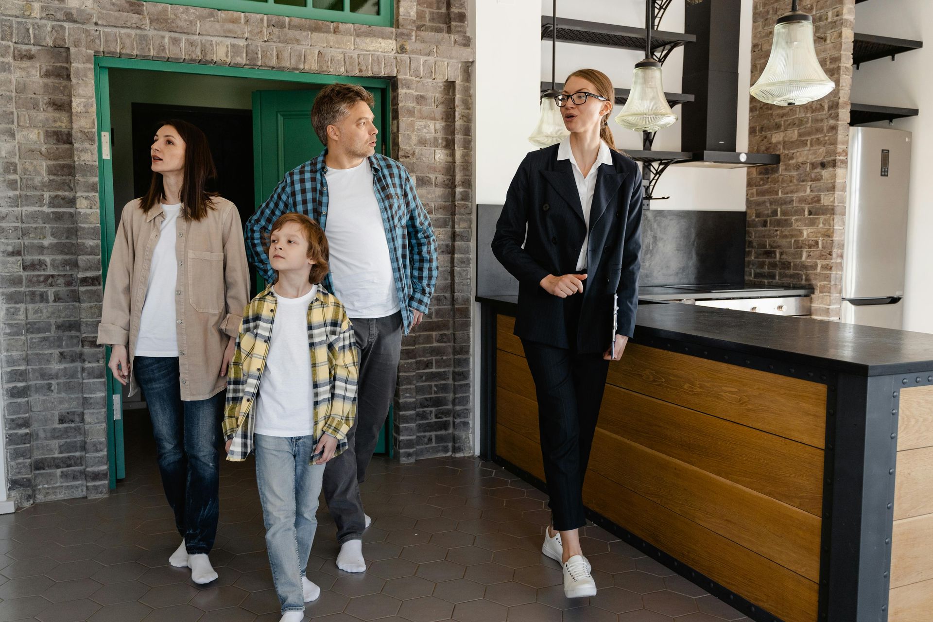 Three people walking into a modern kitchen, with a brick wall and wood island in the background.