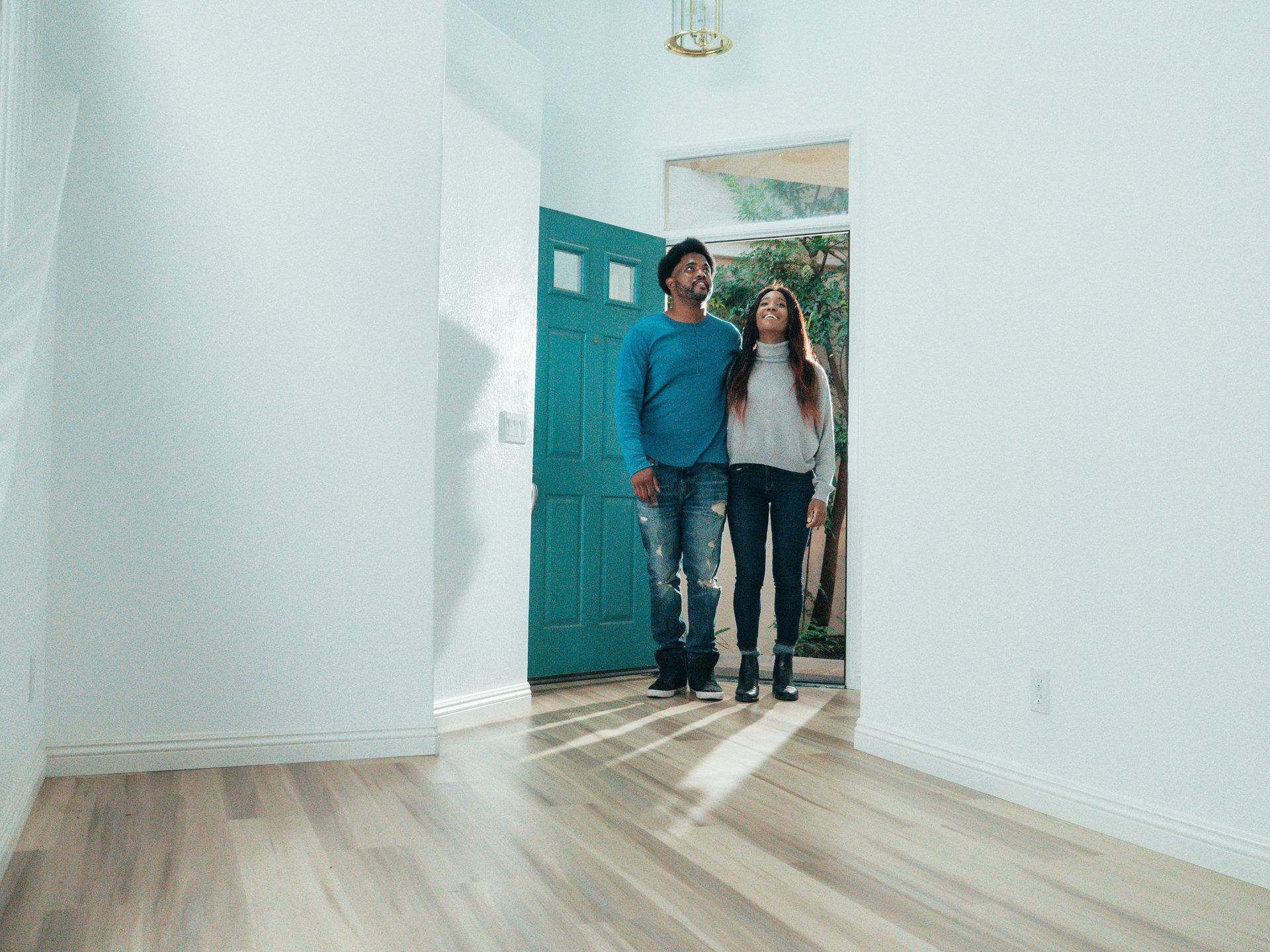 Couple standing in a bright entryway by a teal front door, smiling and embracing.