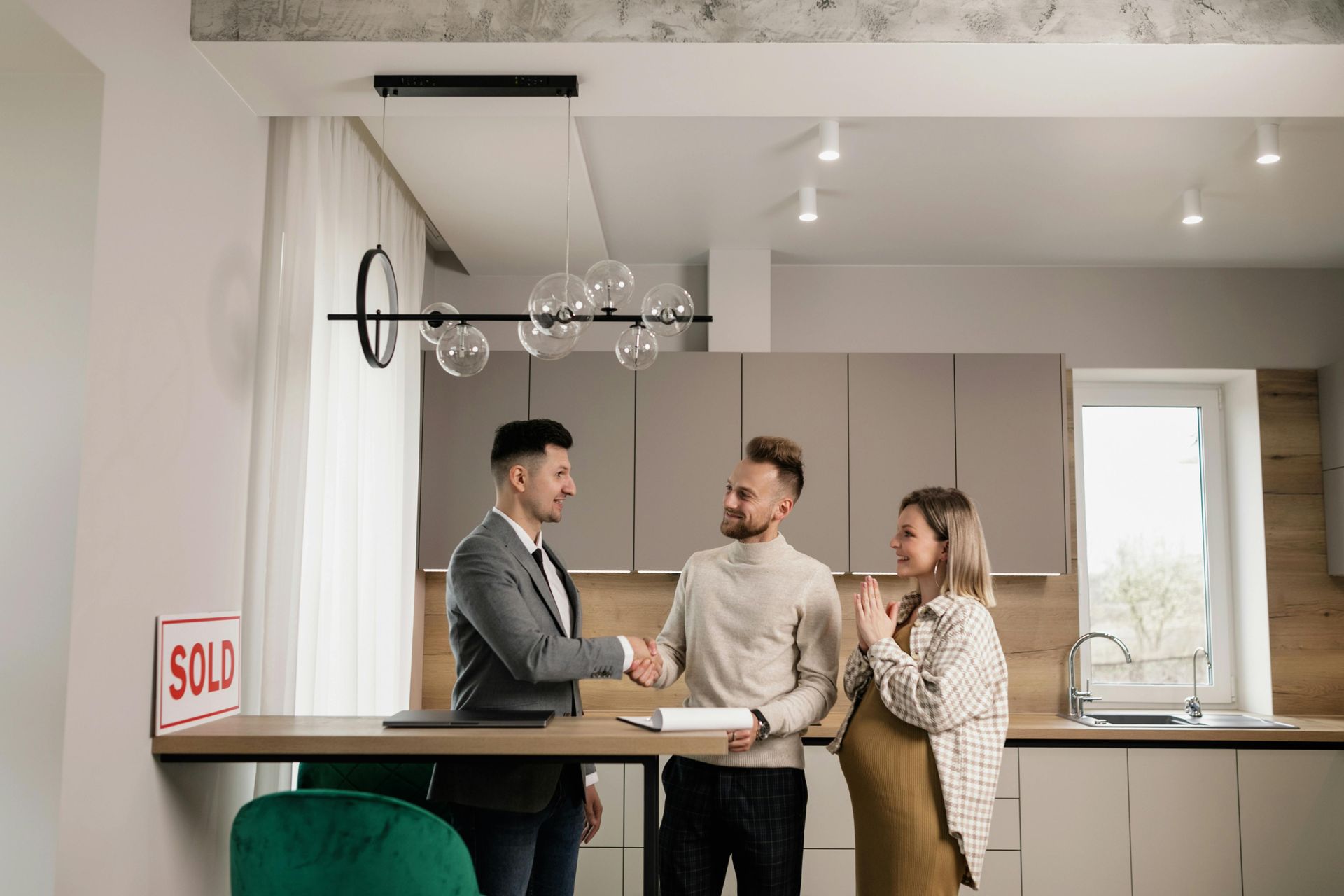 Three people talking in a modern kitchen, with one holding a cup near a countertop.