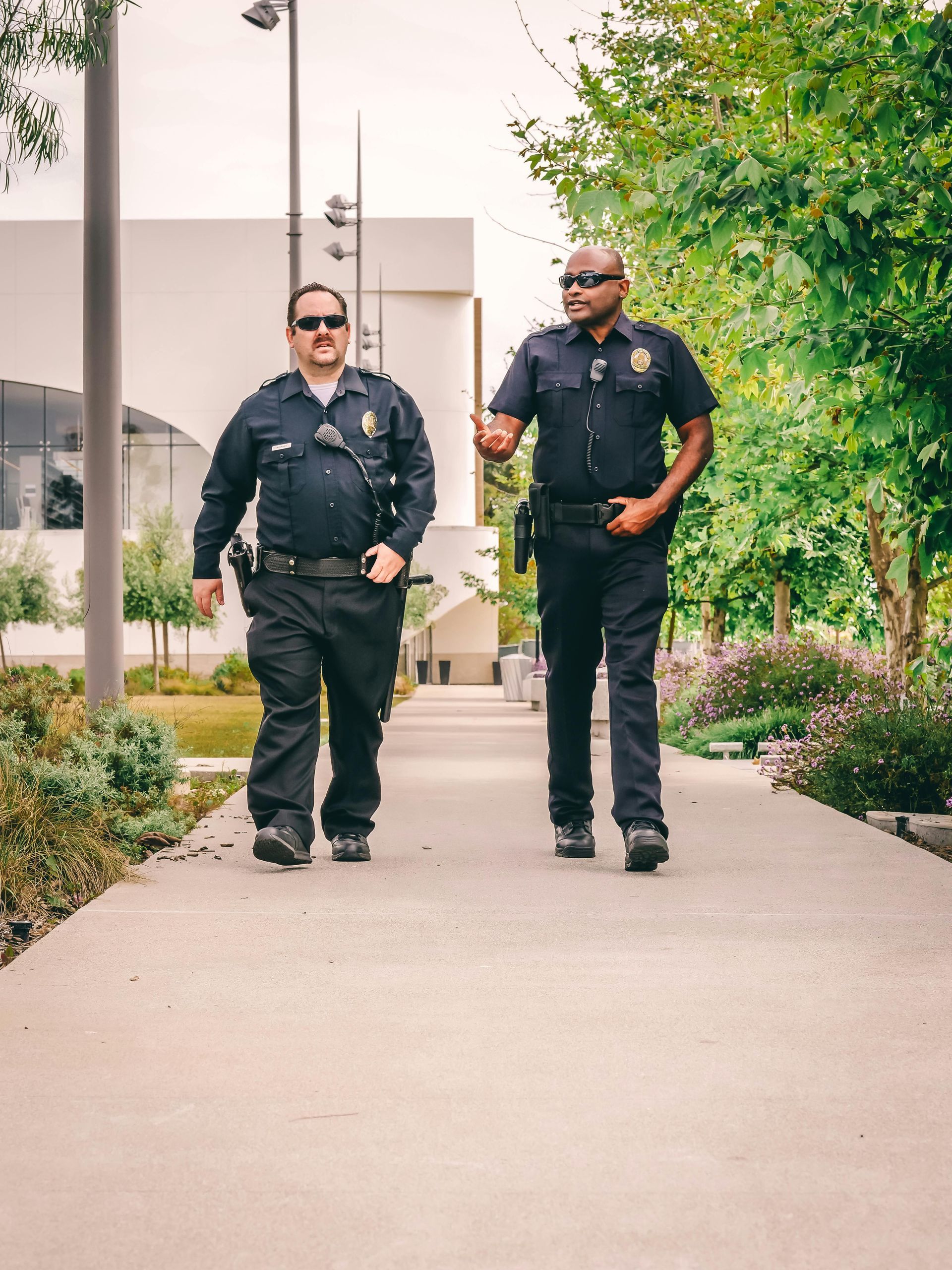 Two male police officers walking on sidewalk.