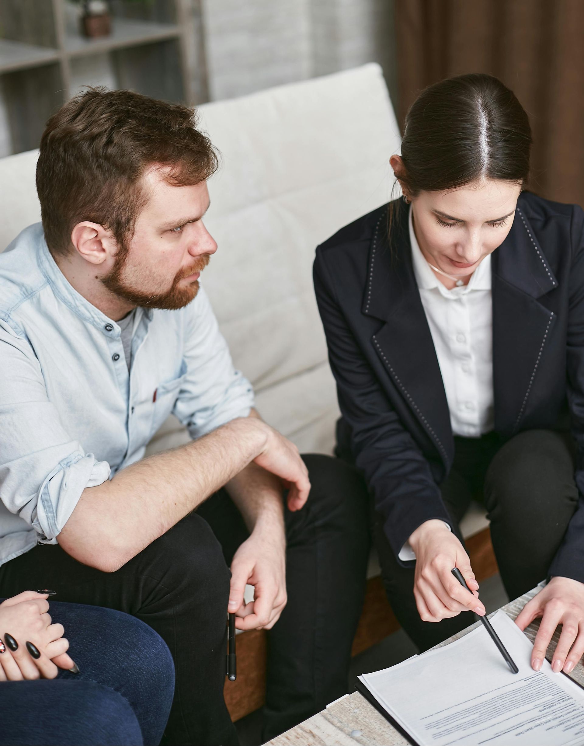 Two people reviewing documents together on a couch, one pointing at a page.