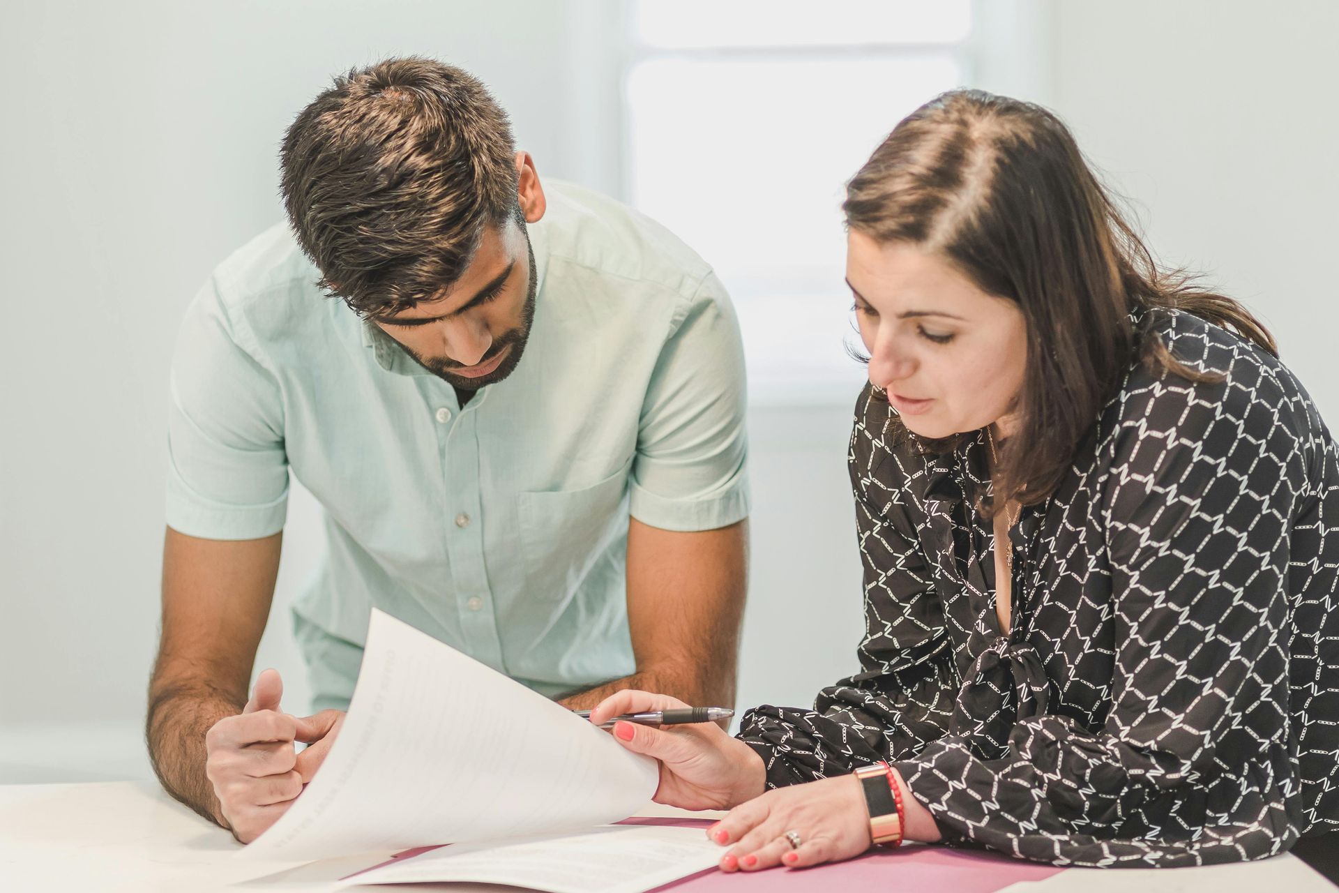 Two people reviewing documents together at a table, discussing a page and pointing at details.