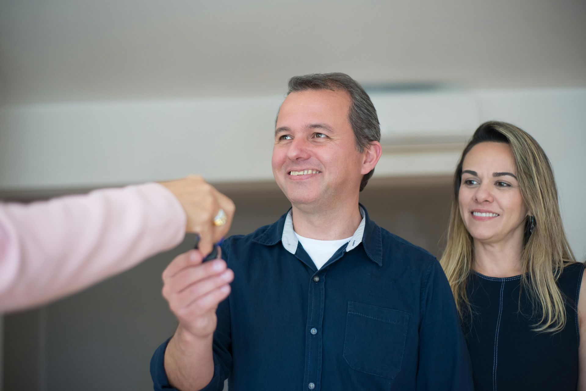 A man receiving house key from a broker, with a woman standing behind him.