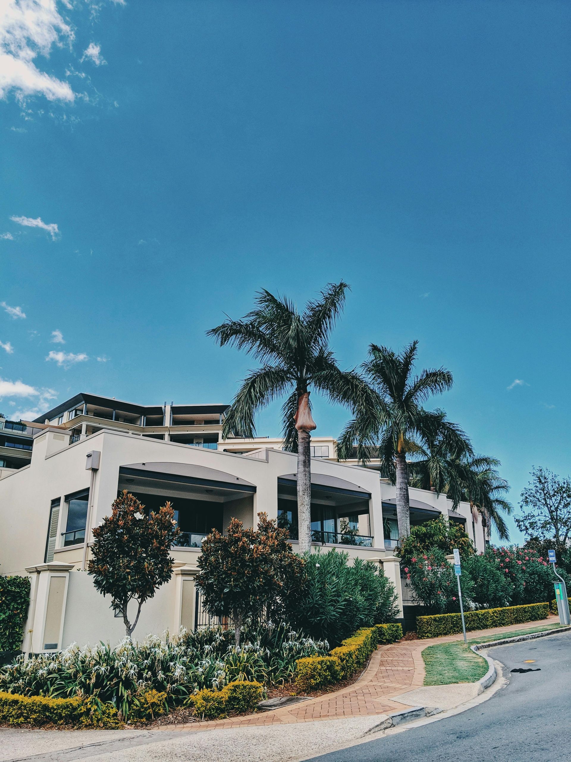 Modern white resort building with palm trees and landscaped curb under a bright blue sky
