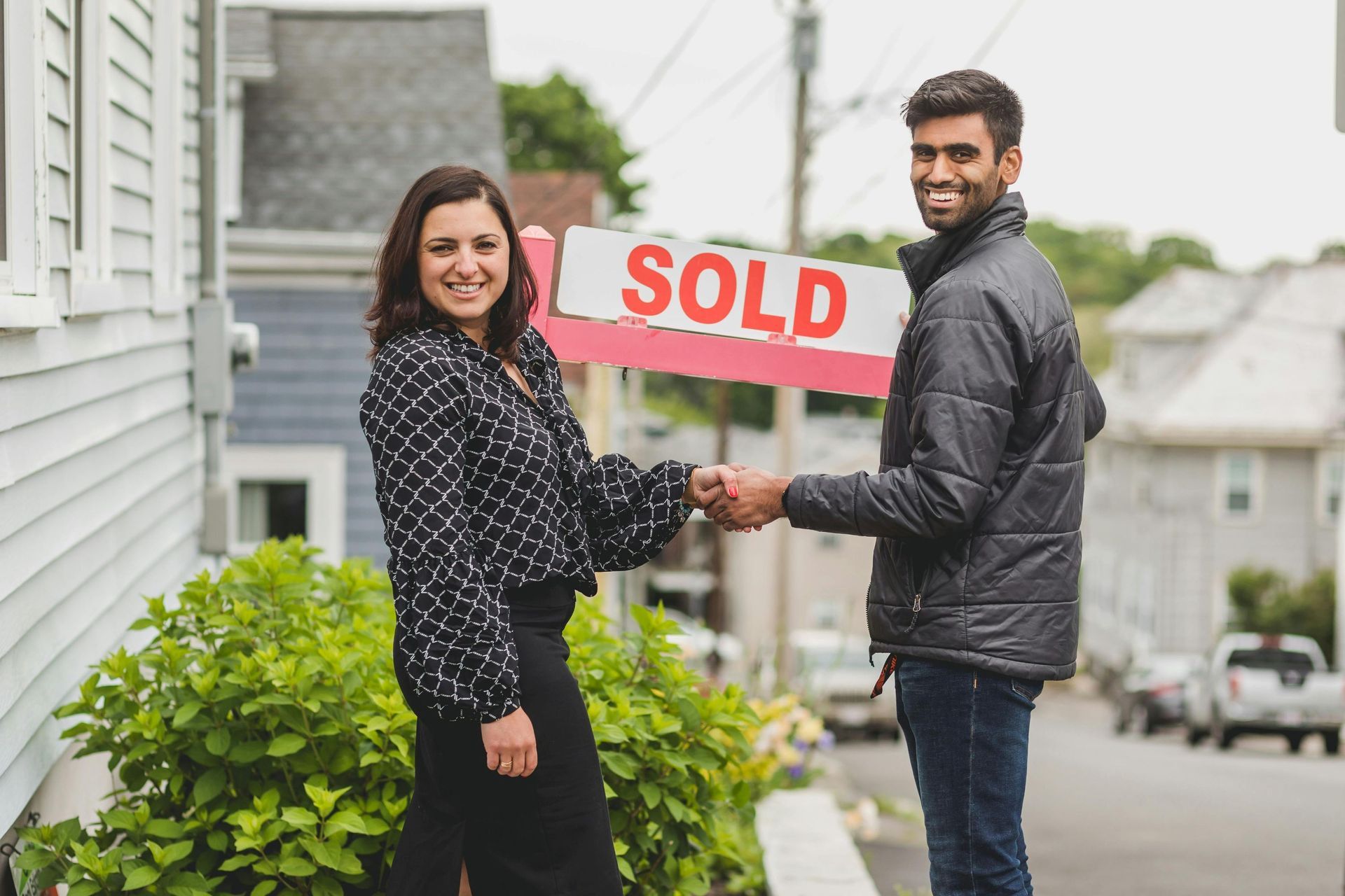 Young man shaking hands with a woman broker outside house that says sold.