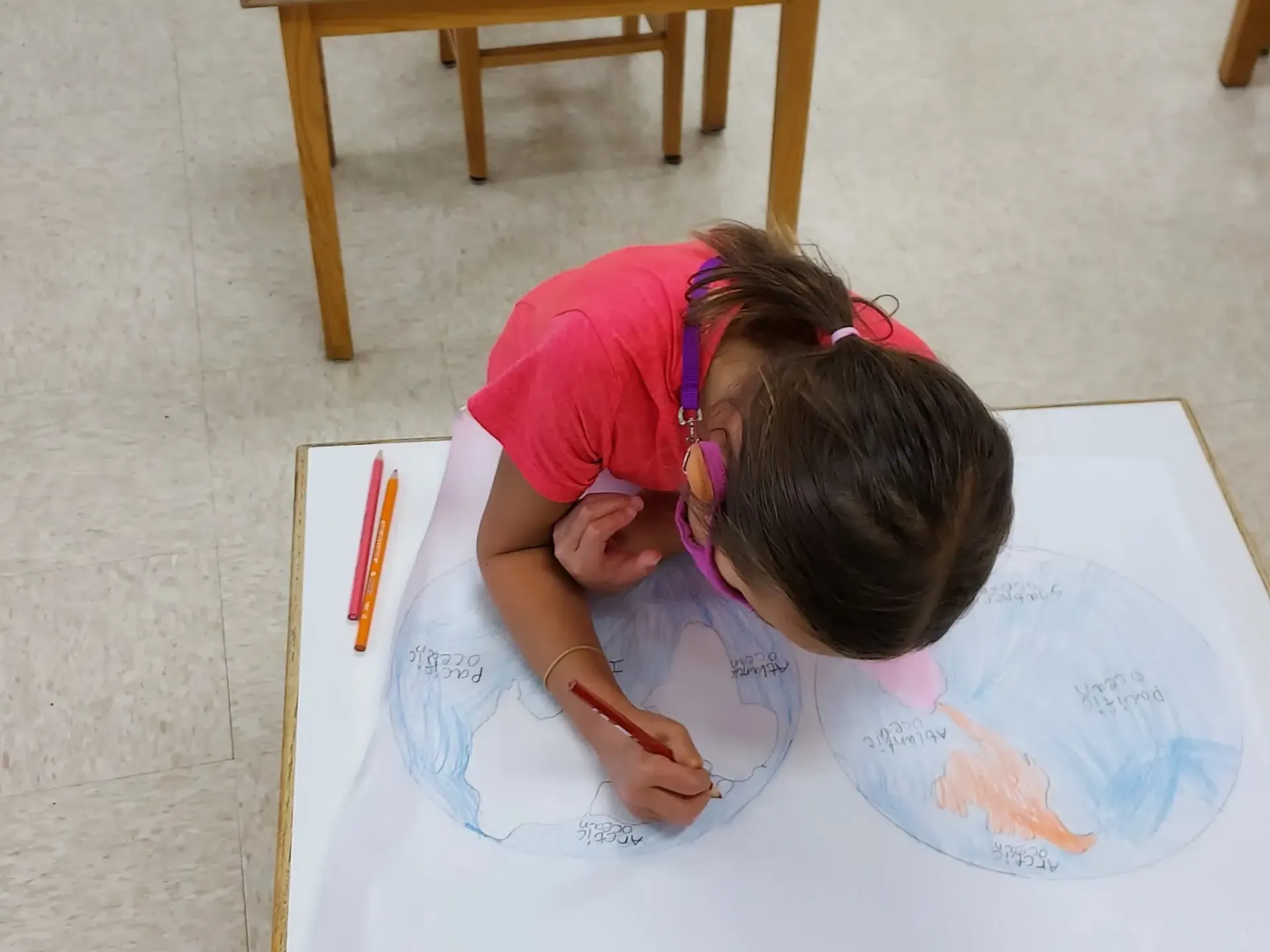 Young person drawing on large paper, using colored pencils at a table.
