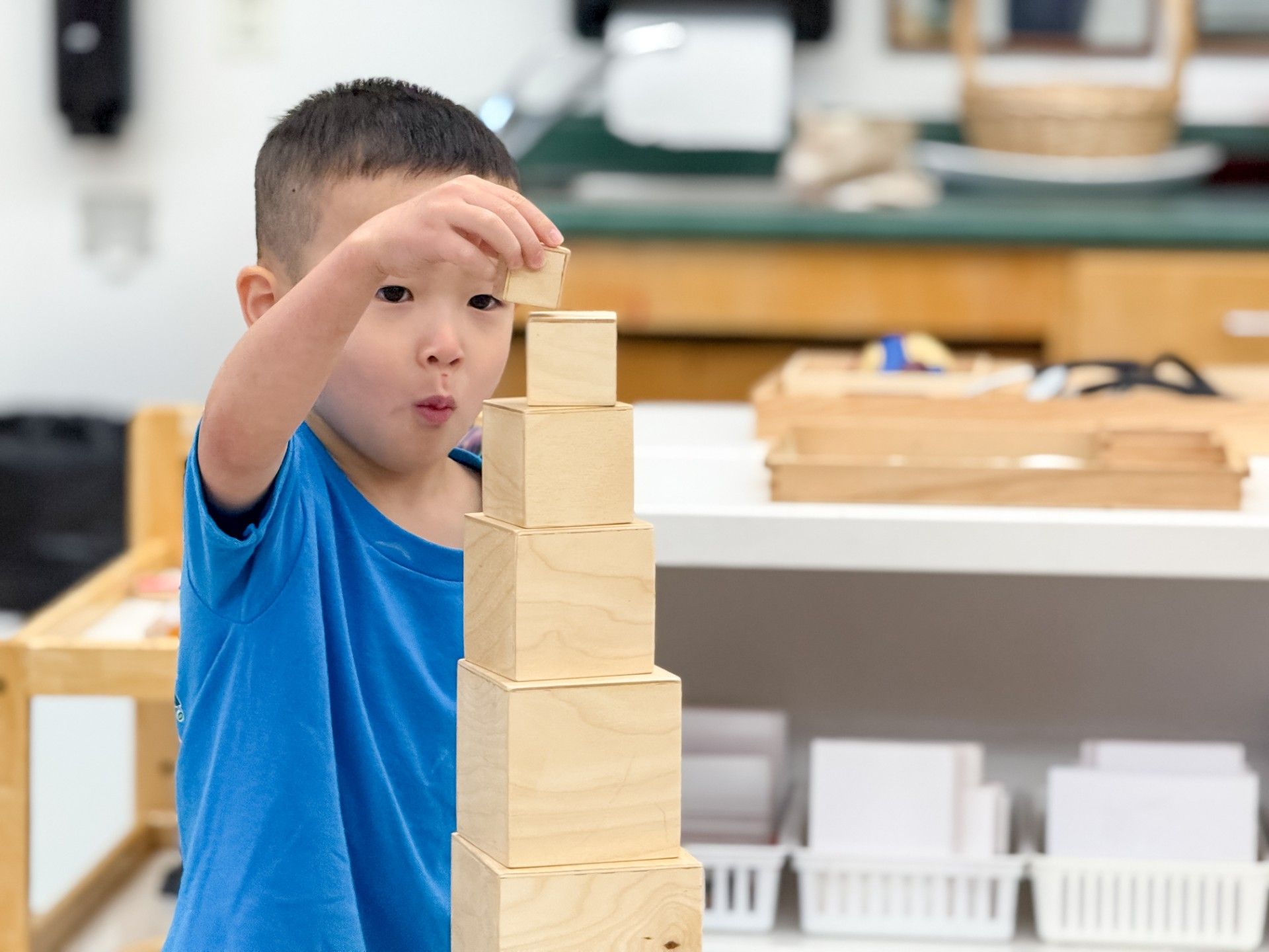 Child placing the smallest block on the top of a stack of wood blocks.