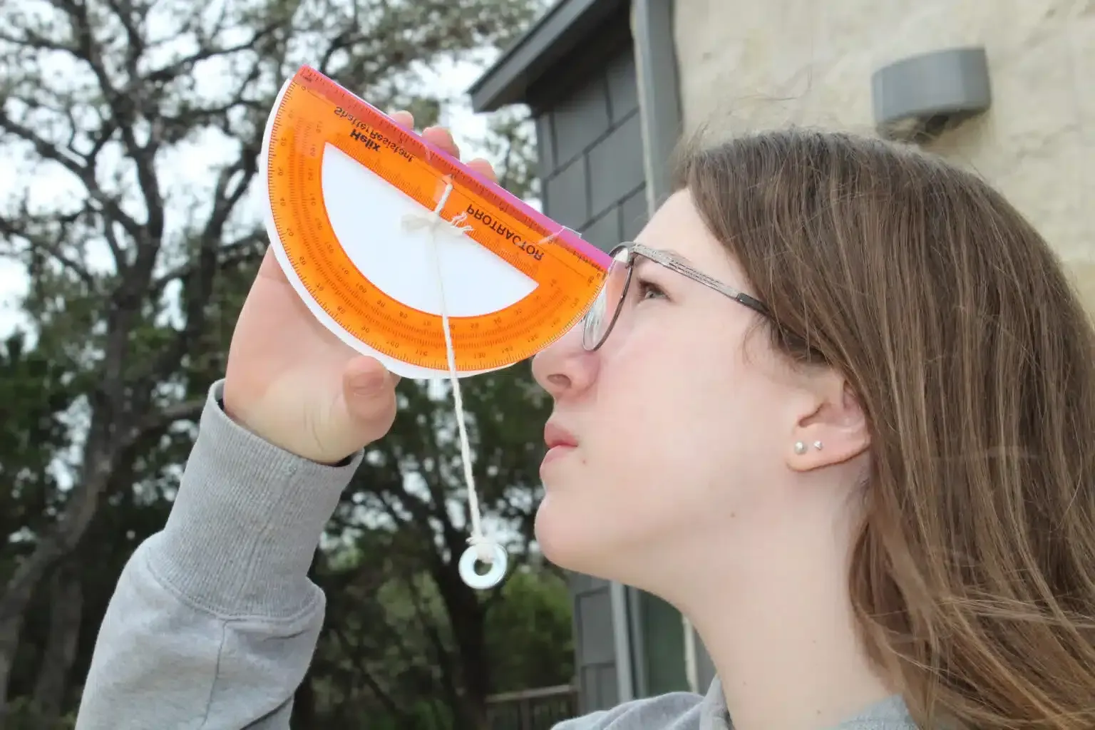 Person using protractor to measure an angle outdoors, cloudy day.