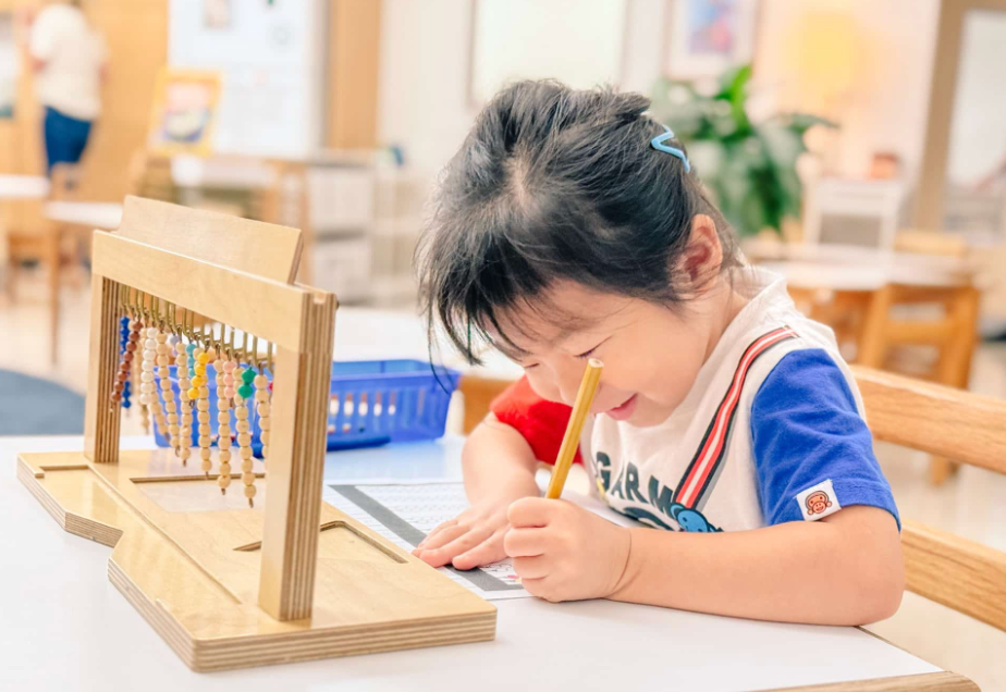 Child using colored pencils, writing at a desk, with a counting frame. Indoors, bright, focused.