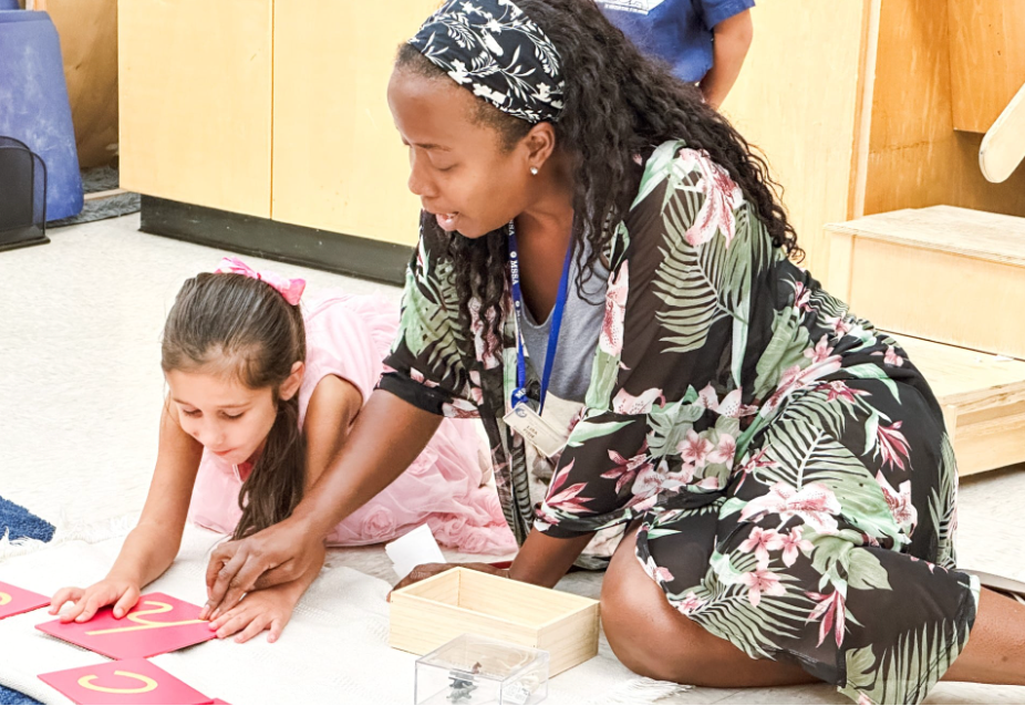 Woman helping a child with letter cards on the floor. Both are focused and engaged in the activity.