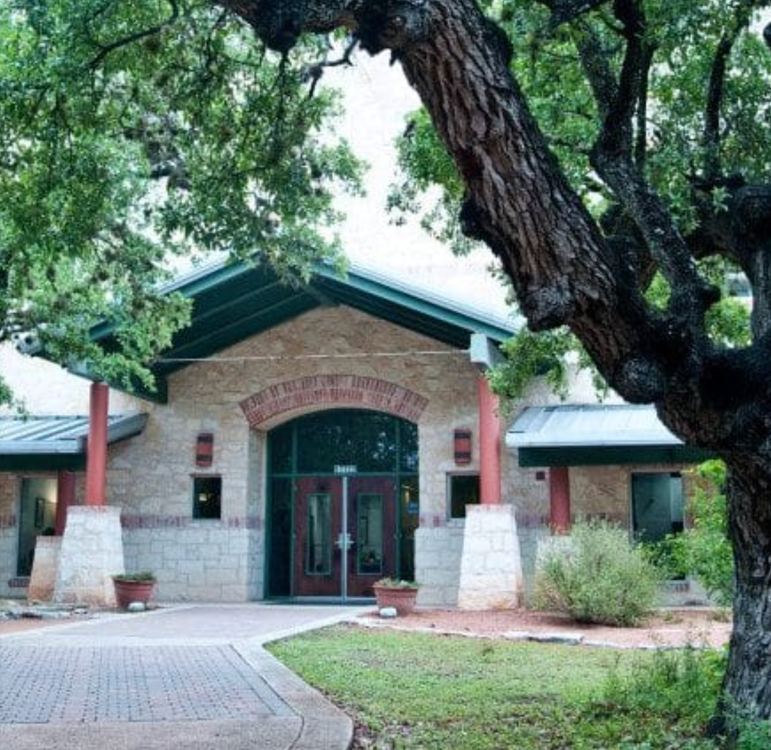 Building exterior with stone walls, brick archway, and double doors, framed by a large tree.