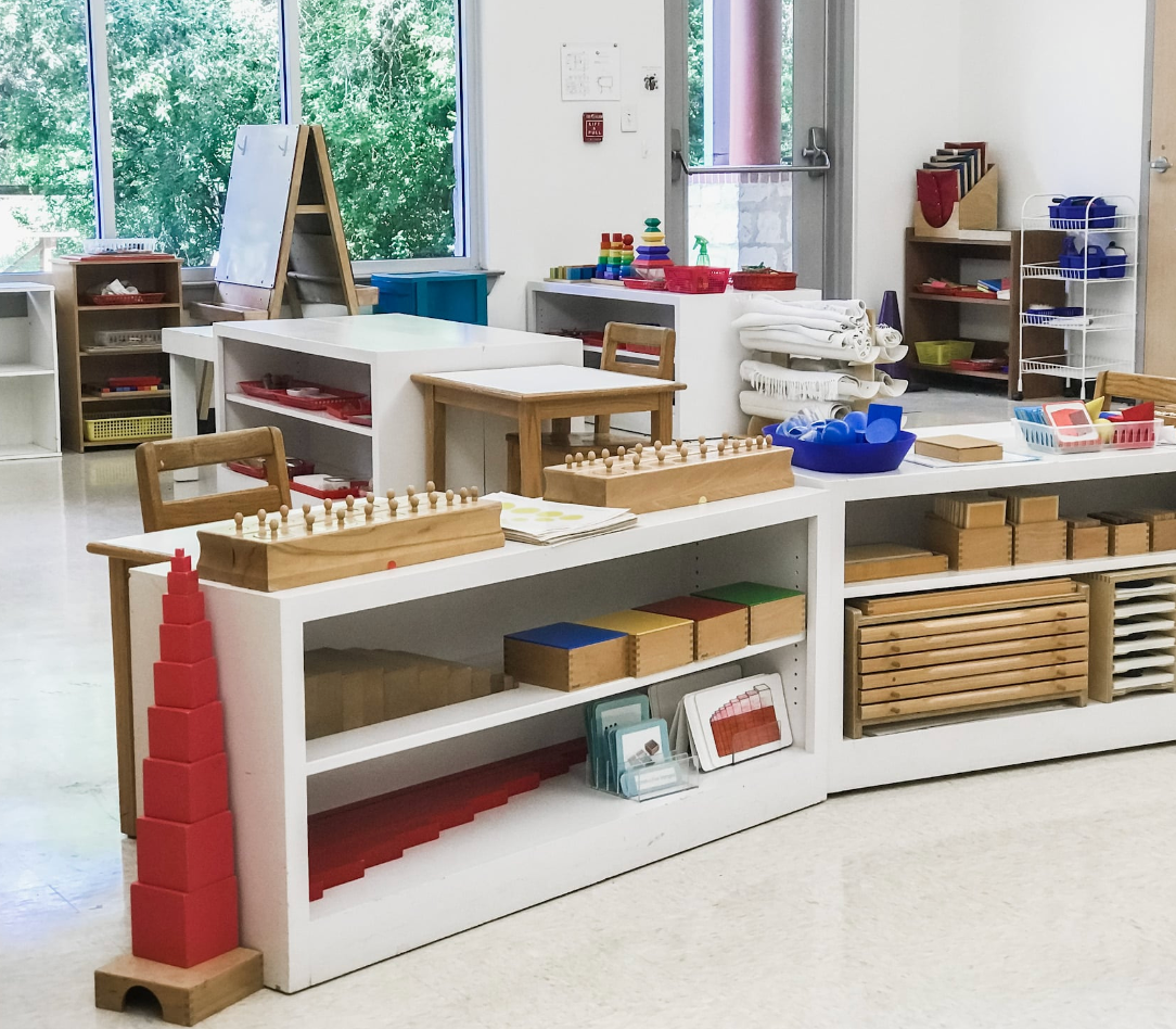 Montessori classroom with shelves displaying educational materials and windows in background.