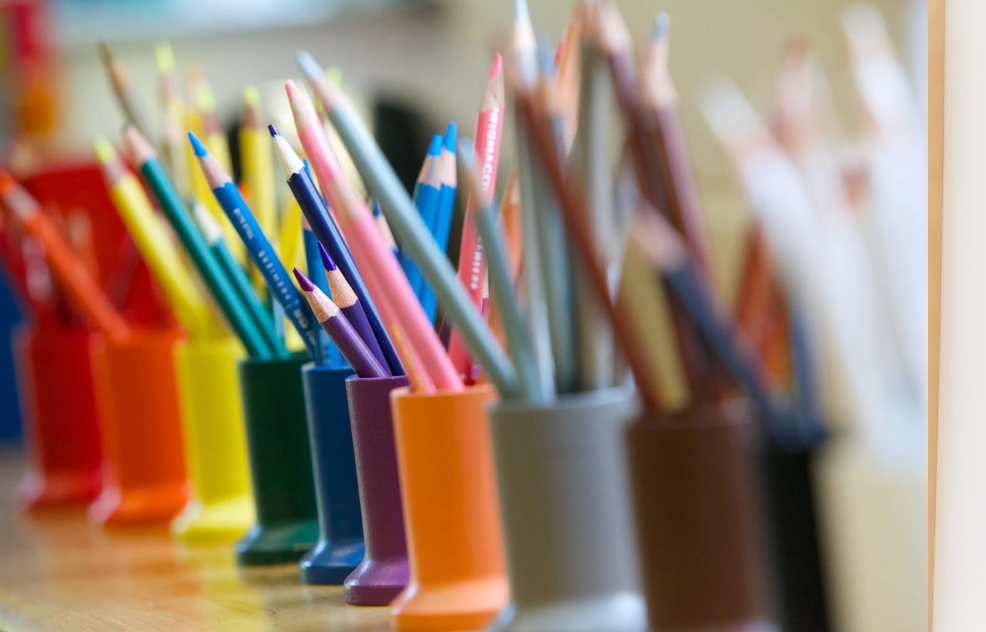 Colorful pencils in a row of small, matching cups, arrayed on a surface.