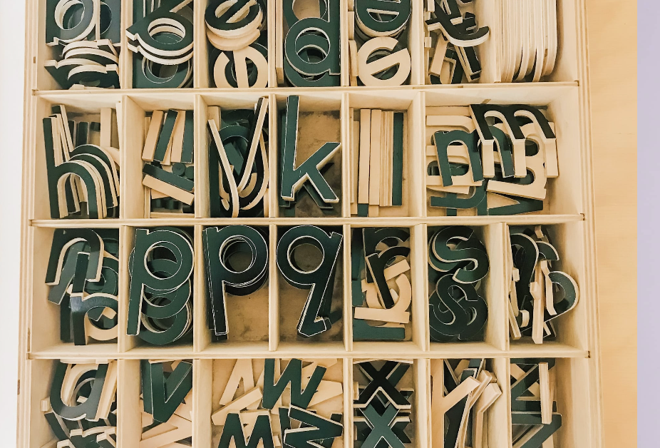 Wooden box with compartments filled with dark green and white wooden letters.