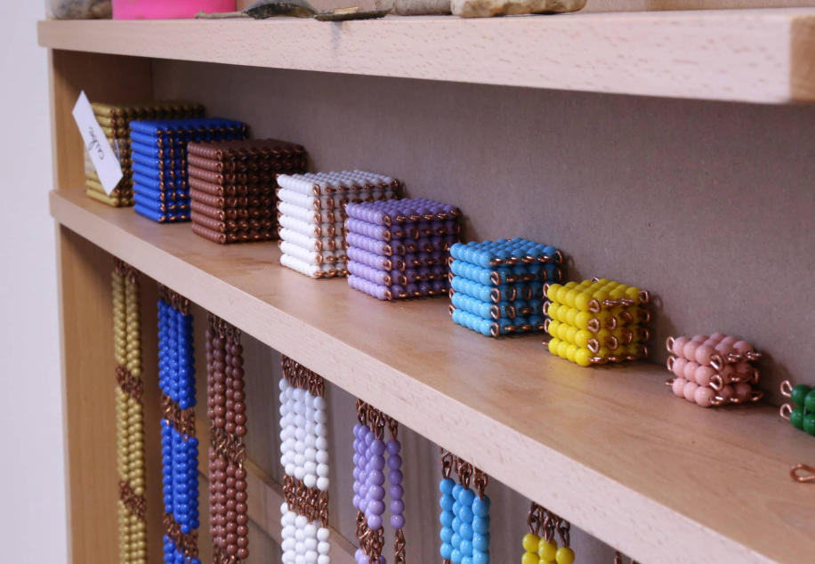 Bead materials on shelves, likely Montessori-style: cubes of various colors and hanging bead chains.
