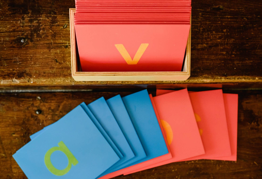 Wooden box with red cards; blue and red cards with letters are spread out.