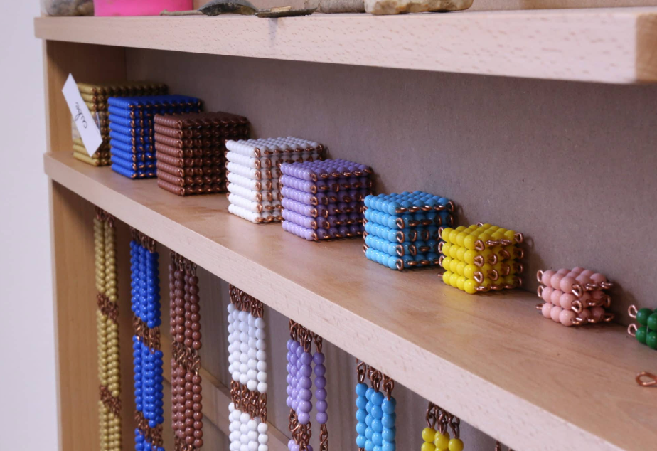 Montessori math materials: beaded cubes and strands in various colors on shelves.