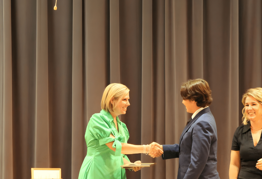 Woman in green dress shakes hands with person in blue suit on stage.