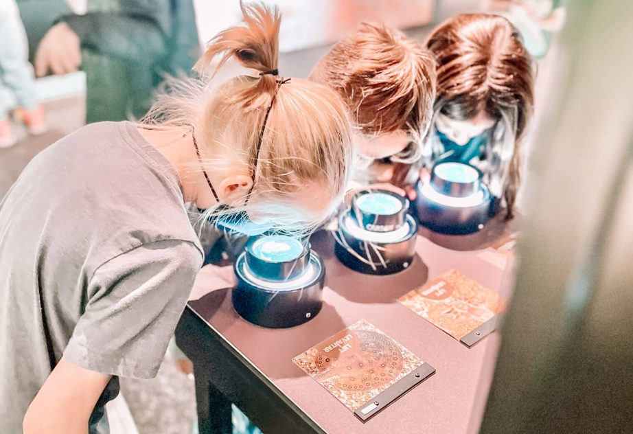 Three people looking closely at lit displays on a table indoors.