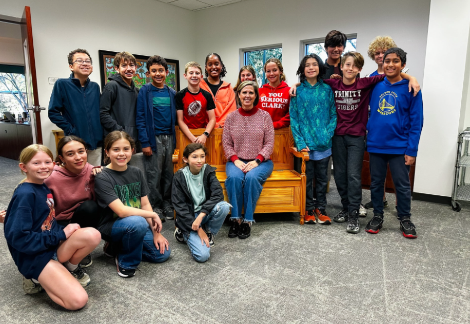 Group of people posing together, likely in a school setting. Some are kneeling, smiling near a wooden bench.