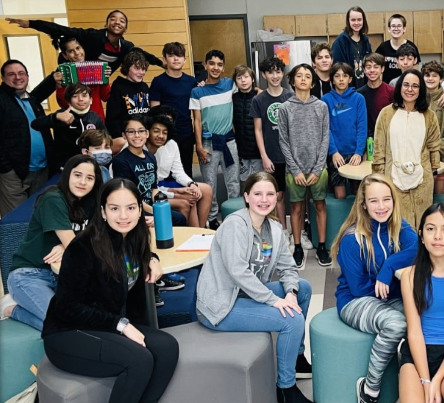 Group of students and adults posing together indoors. Some smiling, wearing casual clothes.