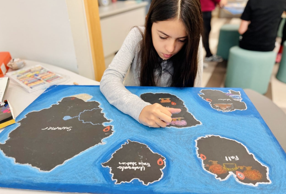 A girl coloring a map with islands on a blue background. She is focused, using a crayon.