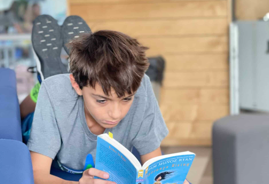 Boy reading book while lying down with feet up.