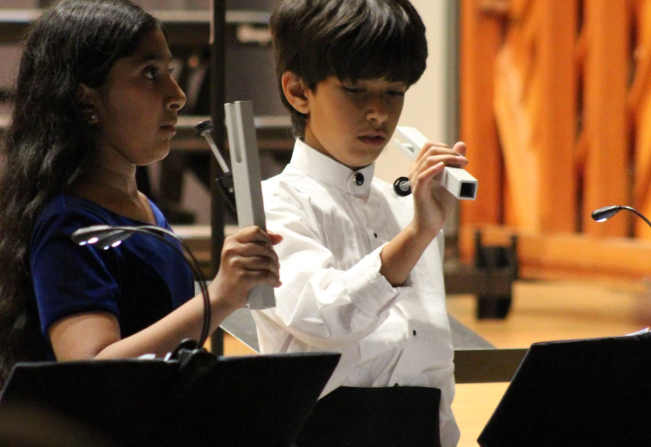 Two children performing with instruments at a concert. Girl with long hair, boy with a white shirt.