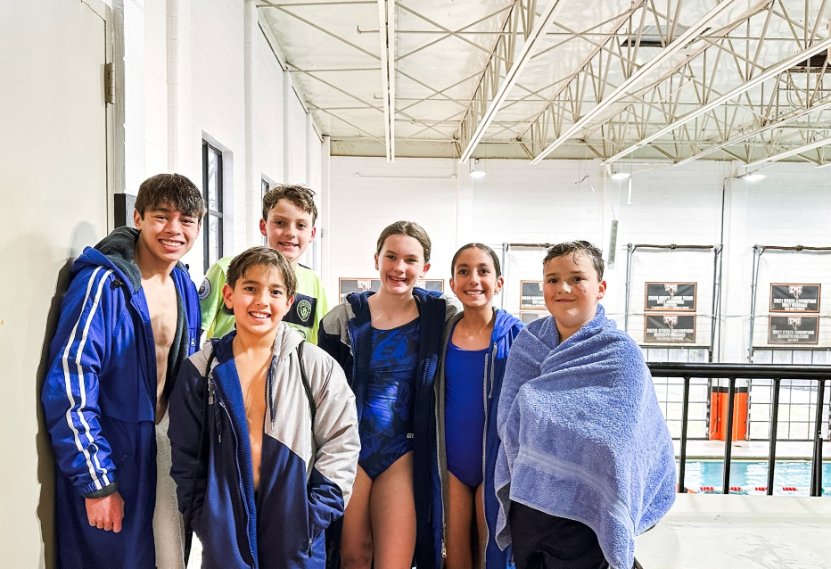 Group of young people in swimsuits and robes by an indoor pool.