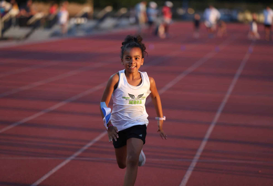 Young runner in white tank top and black shorts sprints on a track.