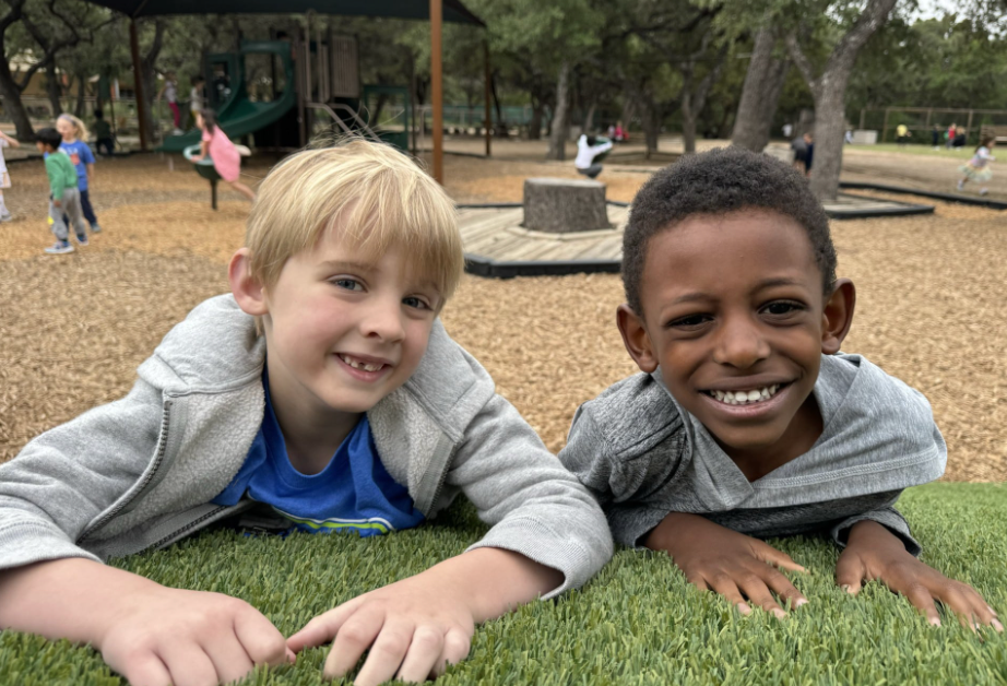 Two boys smiling, lying on artificial grass at a playground.
