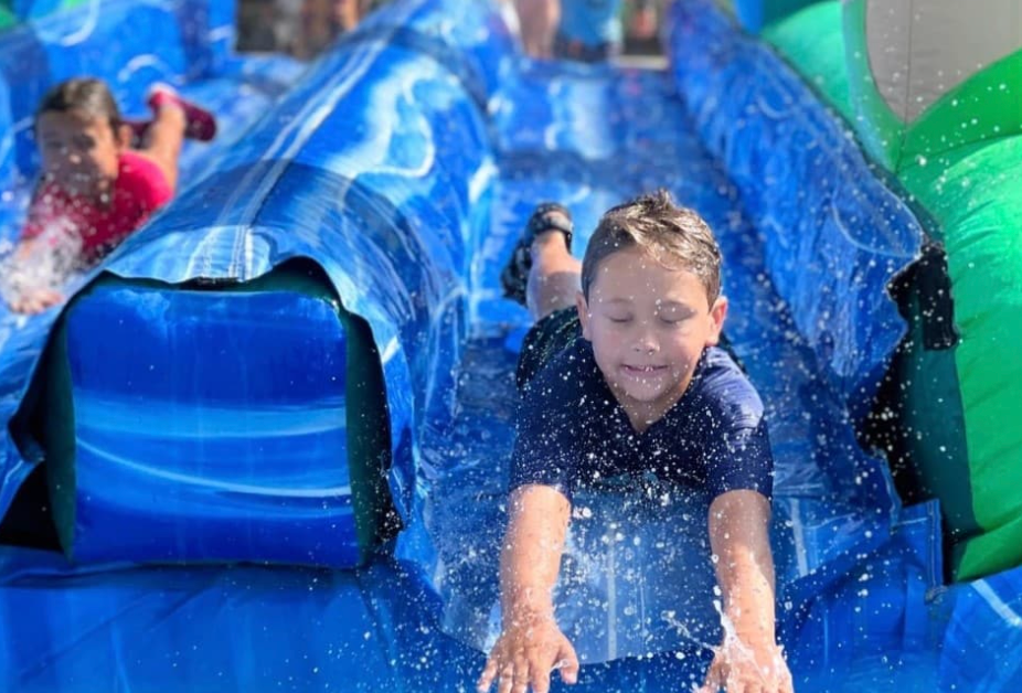Boy sliding down a blue and white water slide, splashing water, smiling.
