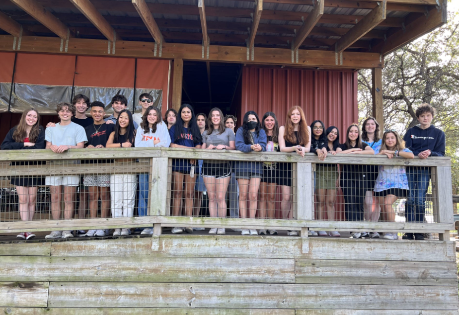 Group of teens pose on a wooden deck in front of a barn.