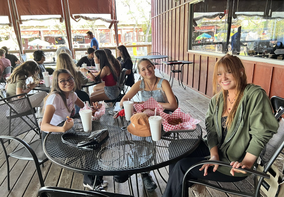 People at outdoor restaurant tables; eating food and smiling.