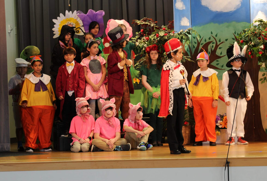 Children in costumes on a stage. Costumes include a rabbit, king, and Mad Hatter.