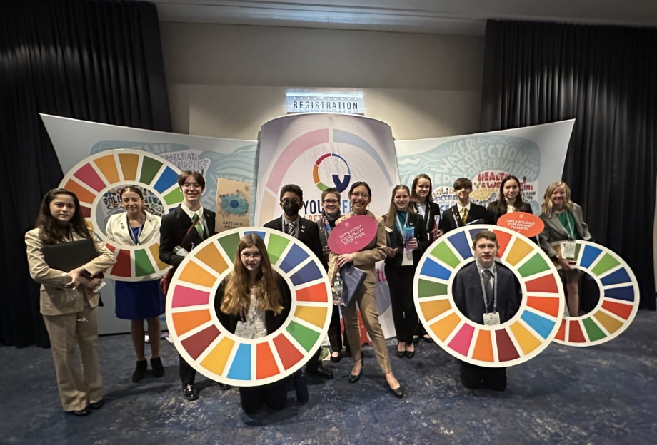 Group holding SDG rings posing in front of backdrop. Bright colors, formal attire.