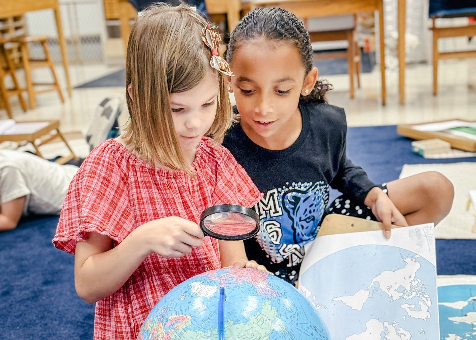Girls using a globe and a magnifying glass to identify countries. 