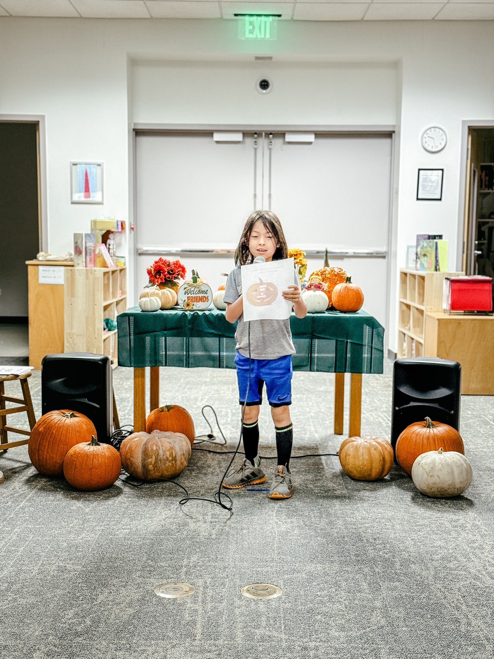 Student presenting his poem with a microphone standing next to pumpkins.