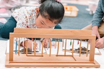 Child using wooden Montessori math beads, intently focused.