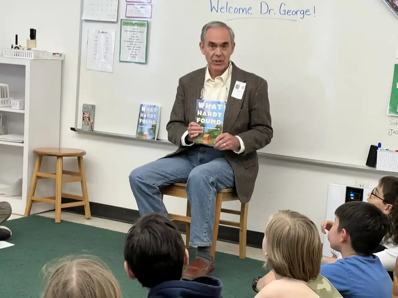 Man reading a book to a group of children in a classroom.